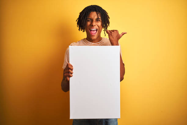 istock Afro american man with dreadlocks holding banner over isolated yellow background pointing and showing with thumb up to the side with happy face smiling 1162385676