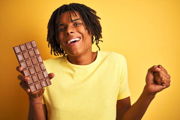 istock Afro american man with dreadlocks eating chocolate bar over isolated yellow background screaming proud and celebrating victory and success very excited, cheering emotion 1162387461