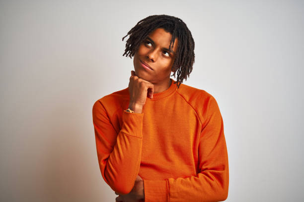 istock Afro american man with dreadlocks wearing orange sweater over isolated white background with hand on chin thinking about question, pensive expression. Smiling with thoughtful face. Doubt concept. 1162387911