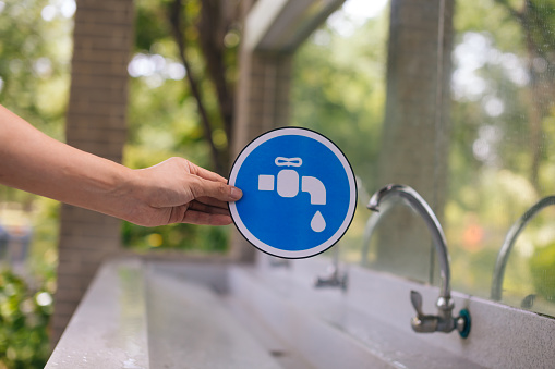 Male hands holding a blue faucet sign with the tap water faucet in the park. Save water and environmental concern concept