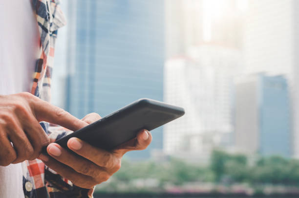 istock close up handsome man using hand typing mobile phones and touch screen working search with app devices outdoor in city with sunrise and building background. 1162390923