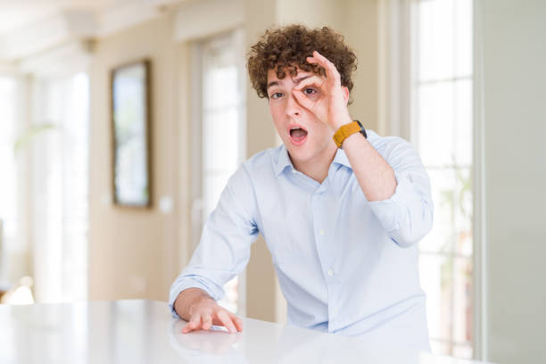 istock Young business man with curly read head doing ok gesture shocked with surprised face, eye looking through fingers. Unbelieving expression. 1162392768