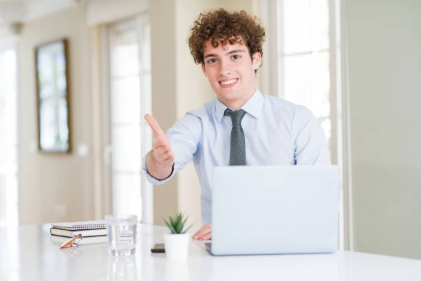 istock Young business man working with computer laptop at the office smiling friendly offering handshake as greeting and welcoming. Successful business. 1162393981
