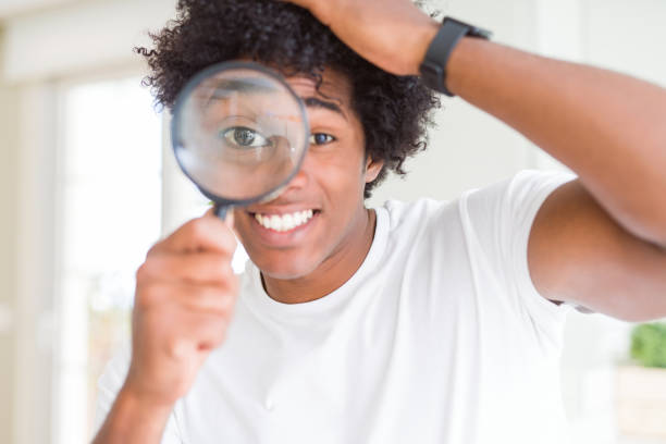 istock African American man looking through magnifying glass stressed with hand on head, shocked with shame and surprise face, angry and frustrated. Fear and upset for mistake. 1162401946
