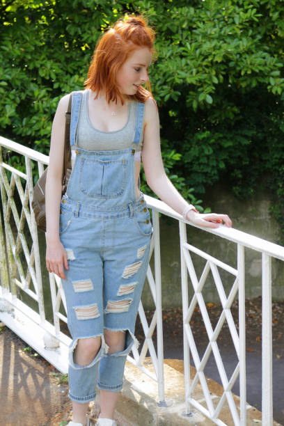 imagem da menina de sorriso feliz do adolescente 14/15 anos velho com cabelo vermelho curto/gengibre bob desgastando do penteado da sarja de nimes azul e o sutiã cinzento dos esportes/bralette, estando na ponte no jardim do parque pelo rio, com a bolsa e  - 16 17 years vibrant color beauty red - fotografias e filmes do acervo