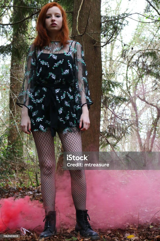 Image Of Moody Teenage Girl With Ginger Red Hair In Woodland Wearing Lbd  Black Party Dress Fishnet Tights Stockings And Leather Boots With Red Smoke  Bomb Teenager With Ginger Bob Hairstyle And