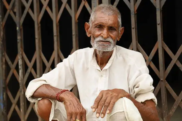 An old man is sitting in dull white clothes.