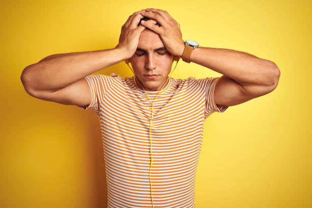istock Young handsome man using headphones over yellow isolated background suffering from headache desperate and stressed because pain and migraine. Hands on head. 1162405414