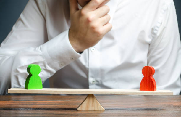istock Man holds his hand on chin looks at the discussion process between red and green figures on a scales. Weighted decision. conflict resolution and the search for a compromise in the dispute. 1162405997