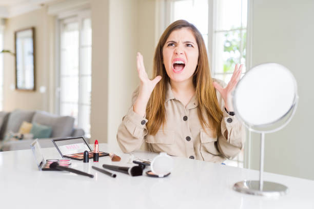 istock Beautiful young woman using make up cosmetics crazy and mad shouting and yelling with aggressive expression and arms raised. Frustration concept. 1162407343