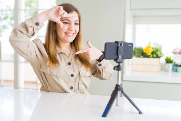 istock Beautiful young woman doing online video call using smartphone webcam smiling making frame with hands and fingers with happy face. Creativity and photography concept. 1162408322