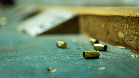 Empty pistol bullet shells on wooden table in a shooting range. Extreme close up and selective focus with blur background.