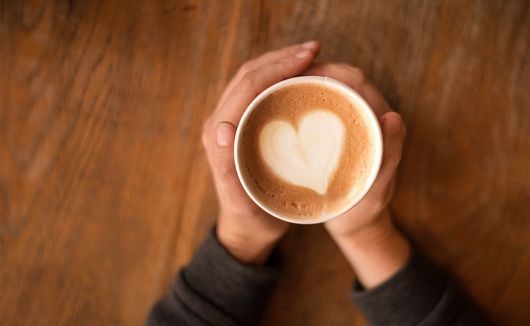 Close-up of female hands holding cup of coffee at cafe table