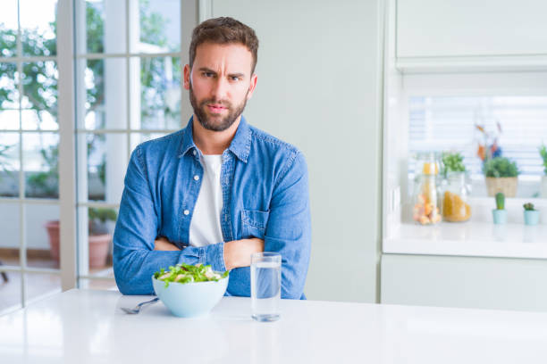 istock Handsome man eating fresh healthy salad skeptic and nervous, disapproving expression on face with crossed arms. Negative person. 1162410579