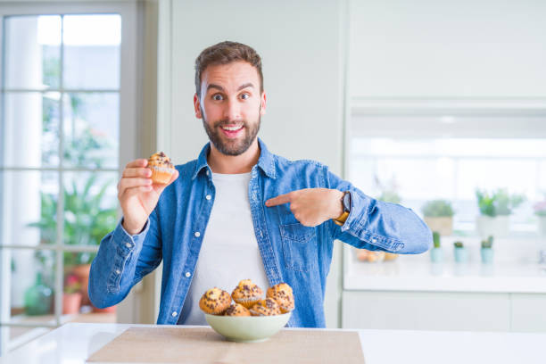 istock Handsome man eating chocolate chips muffin with surprise face pointing finger to himself 1162411347