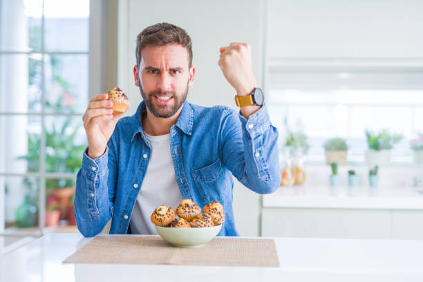 istock Handsome man eating chocolate chips muffin annoyed and frustrated shouting with anger, crazy and yelling with raised hand, anger concept 1162411357