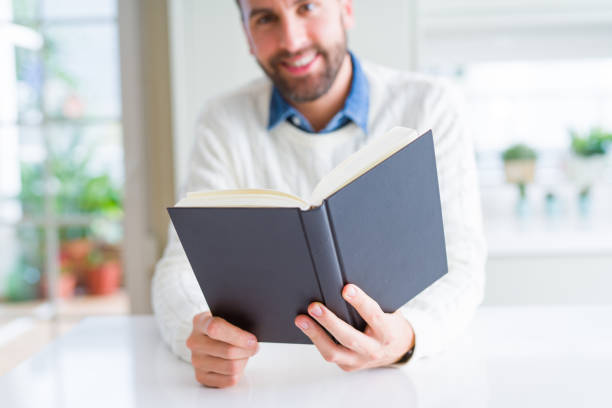 istock Handsome man reading a book at home 1162411923