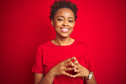 Young beautiful african american woman with afro hair over isolated red background Hands together and fingers crossed smiling relaxed and cheerful. Success and optimistic