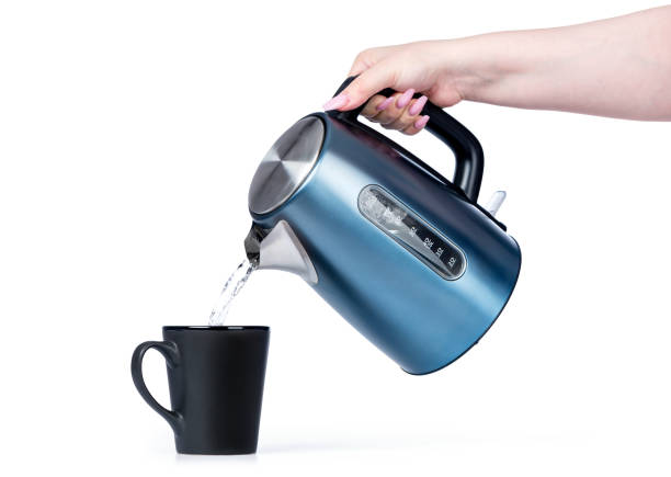 istock Female hand pours water from a kettle into a black mug, isolated on white background. File contains a path to isolation. 1162416016
