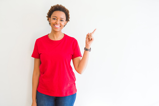 Young beautiful african american woman over white background with a big smile on face, pointing with hand and finger to the side looking at the camera.