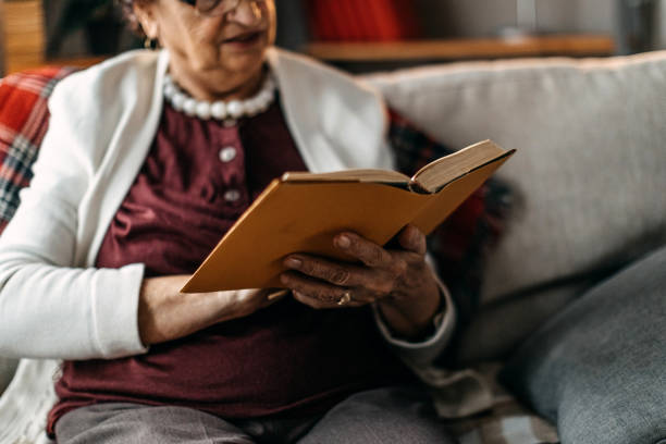istock Old woman sitting on sofa and reading a book 1162423965