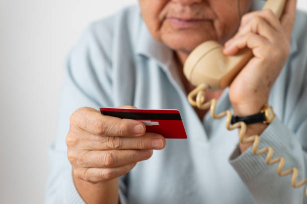 Senior Woman With Credit Card Senior woman using phone while holding credit card. white collar crime stock pictures, royalty-free photos & images