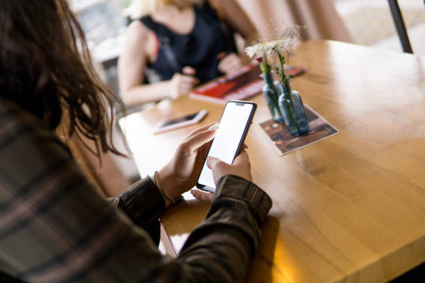 istock Girl using a mobile phone while out with her friend in a cafe, using a smart phone indoor to send a text message, checking social media, chatting online with wifi wireless 1162425081