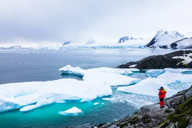 Photo of Tourist taking photos of amazing frozen landscape in Antarctica with icebergs, snow, mountains and glaciers, beautiful nature in Antarctic Peninsula with ice
