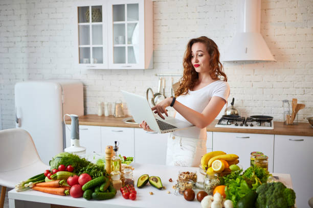 istock Young beautiful woman using a notebook while cooking in the modern kitchen. Healthy food and Dieting concept. Losing Weight 1162432426