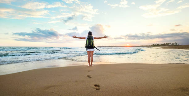 Woman backpacker greeting a sunset at the ocean coast stock photo
