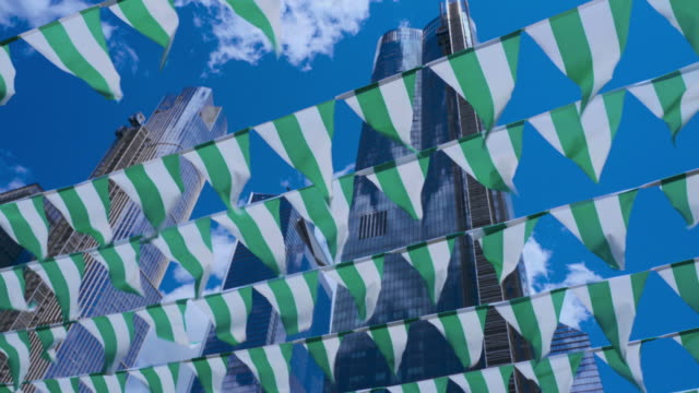 Decorative flags flying on the wind against a blue sky, with skyscrapers in the backdrop. High Line Park, Manhattan, New York City, USA