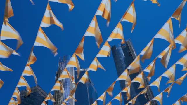 Decorative flags flying on the wind against a blue sky, with skyscrapers in the backdrop. High Line Park, Manhattan, New York City, USA
