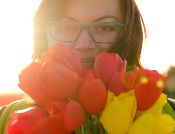 Young adult female holding bouquet of tulips, smiling and looking at camera