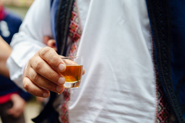 close up on midsection of man in serbian national folk costume holding a glass of rakia homemade brandy drink slivovitza outdoors day - slivovitz imagens e fotografias de stock