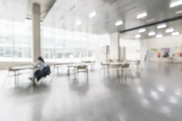 Photo of Office building or university lobby hall blur background with blurry school hallway corridor interior view toward empty corridor entrance, glass curtain wall, floor and exterior light illumination