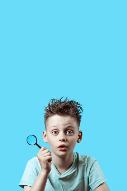 istock a boy in a light t-shirt holding a small magnifying glass on blue background 1162456344