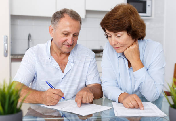 istock Smiling mature couple  at table in home kitchen filling up documents 1162457632