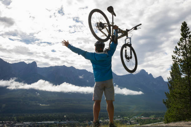 istock Mountain biker holds bicycle overhead in mountain meadow 1162458856