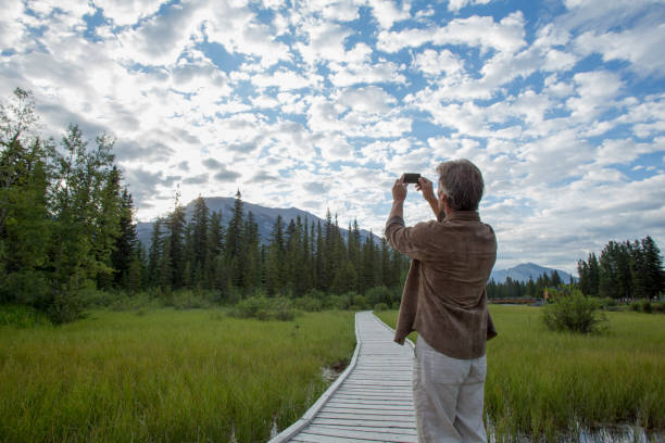 istock Man uses cell phone to take photograph along boardwalk 1162458932