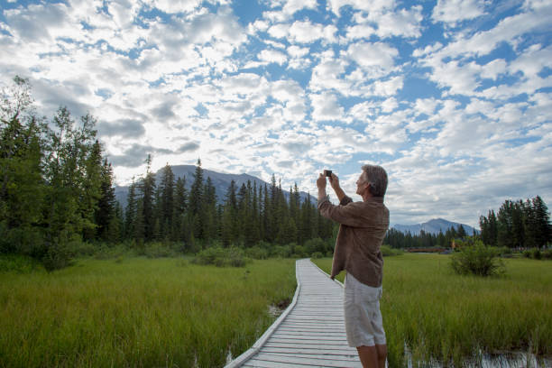 istock Man uses cell phone to take photograph along boardwalk 1162458933
