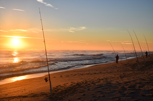 Sunrise on a Florida beach with surf fishing poles and a fisherman silhouette.