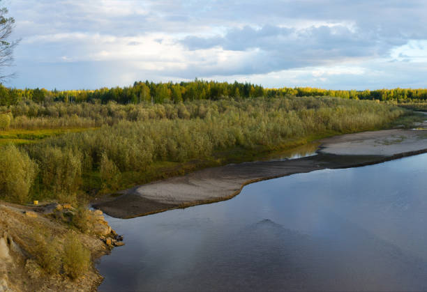 istock Bright sunset with reflection in water clouds a small river Kempendyay in Yakutia off a cliff and spruce forests in the wild North of the track and the descent to the water. 1162461685