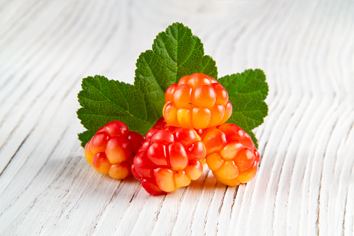 few berries of cloudberries with a leaf on an white wooden board close-up.