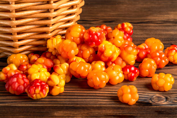 manciata di bacche di cloudberry versate da un piccolo cesto su una vecchia tavola di legno da vicino - karelia foto e immagini stock