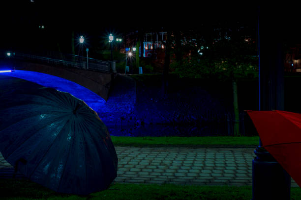 istock Night park after the rain with illuminated bridge and lighted black and red umbrellas. Underexposed photo. 1162465662