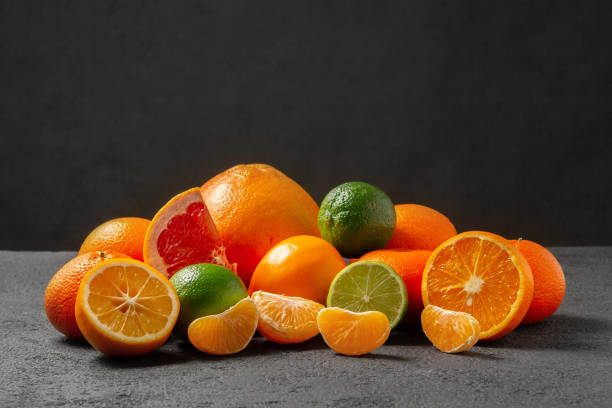 group of citrus fruits - tangerines, lemons, limes, oranges, grapefruits on the surface of a gray table against a black wall - image with copy space
