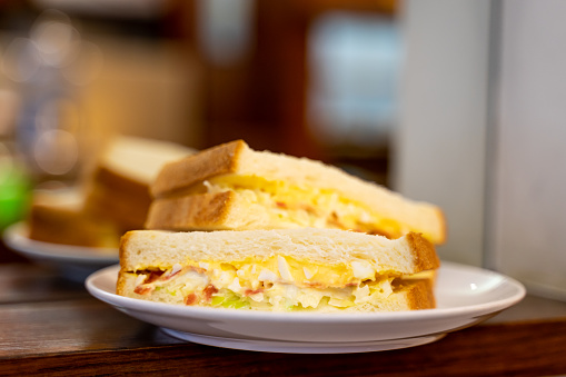 Closed up of morning sandwiches with egg, ham and vegetable on white dish in coffee shop.