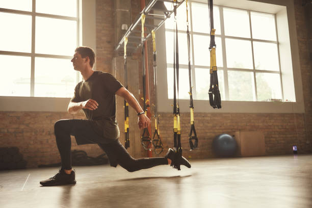 TRX Training. Young athletic man in sports clothing training legs with trx fitness straps in the gym TRX Training. Young athletic man in sports clothing training legs with trx fitness straps in the gym. Sport concept. Workout suspension training stock pictures, royalty-free photos & images