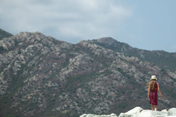 A young girl with a hat standing with her back to the camera looking at the mountain background