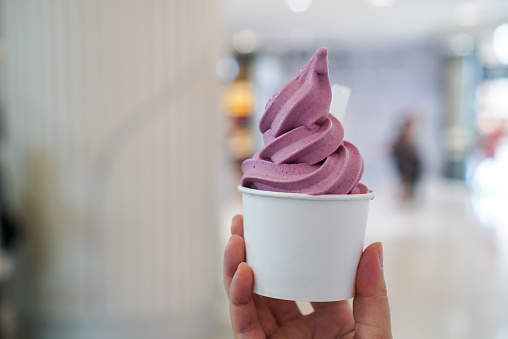 Woman holding a cup of soft serve ice cream with yogurt sweet potato flavour. (isolated)